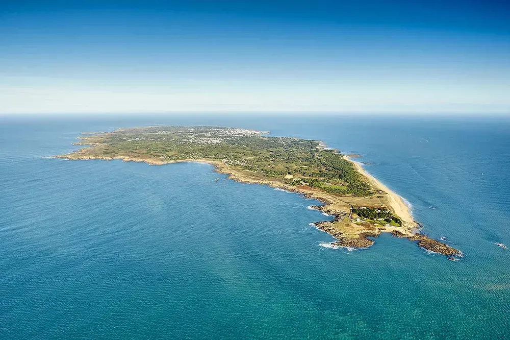 Vue aérienne panoramique de l'Île d'Yeu entourée d'une mer turquoise sous un ciel bleu.