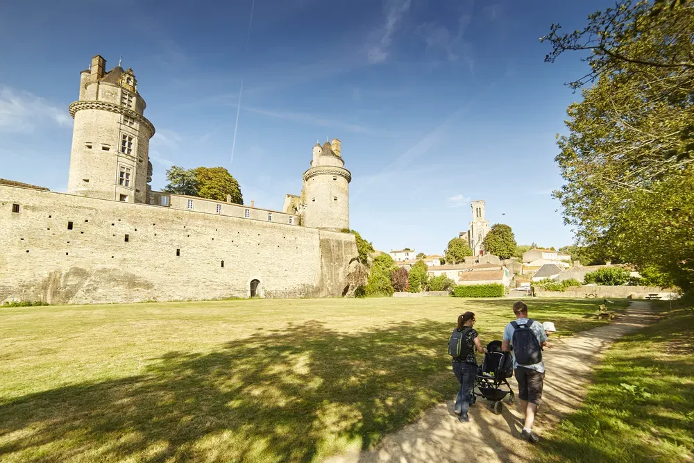 Une famille avec une poussette se promène dans le grand parc verdoyant au pied des remparts du château d'Apremont